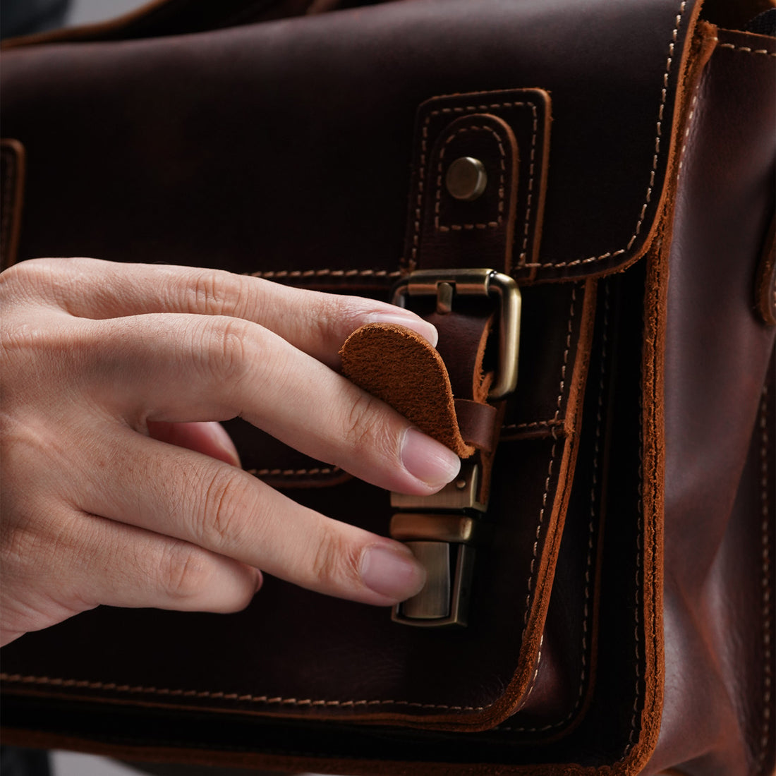 Close view of the antique-tone front buckle on the leather satchel