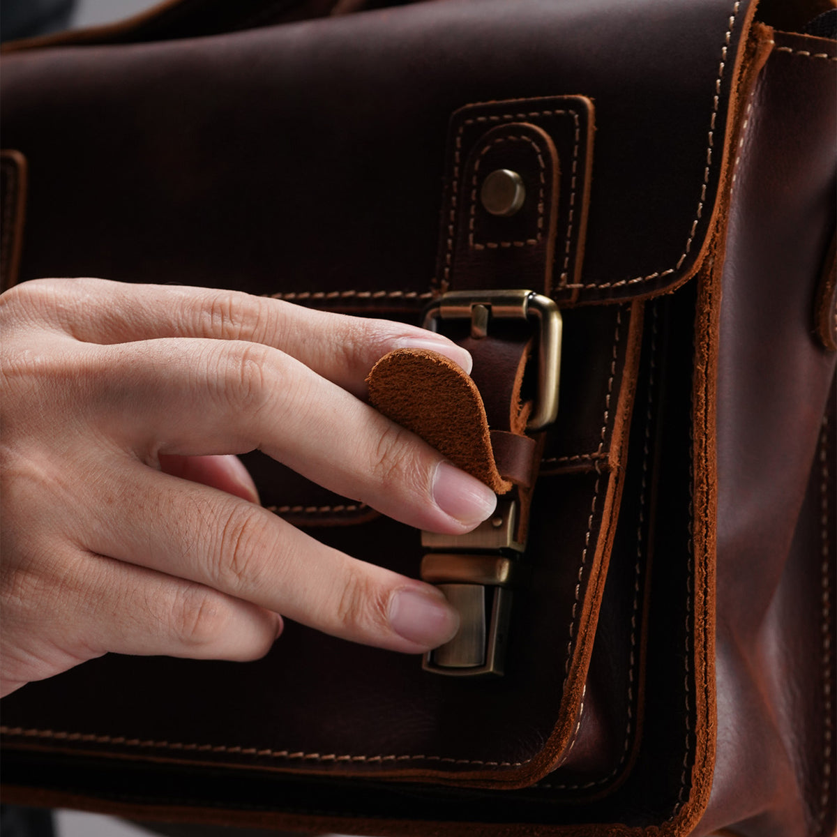 Close view of the antique-tone front buckle on the leather satchel