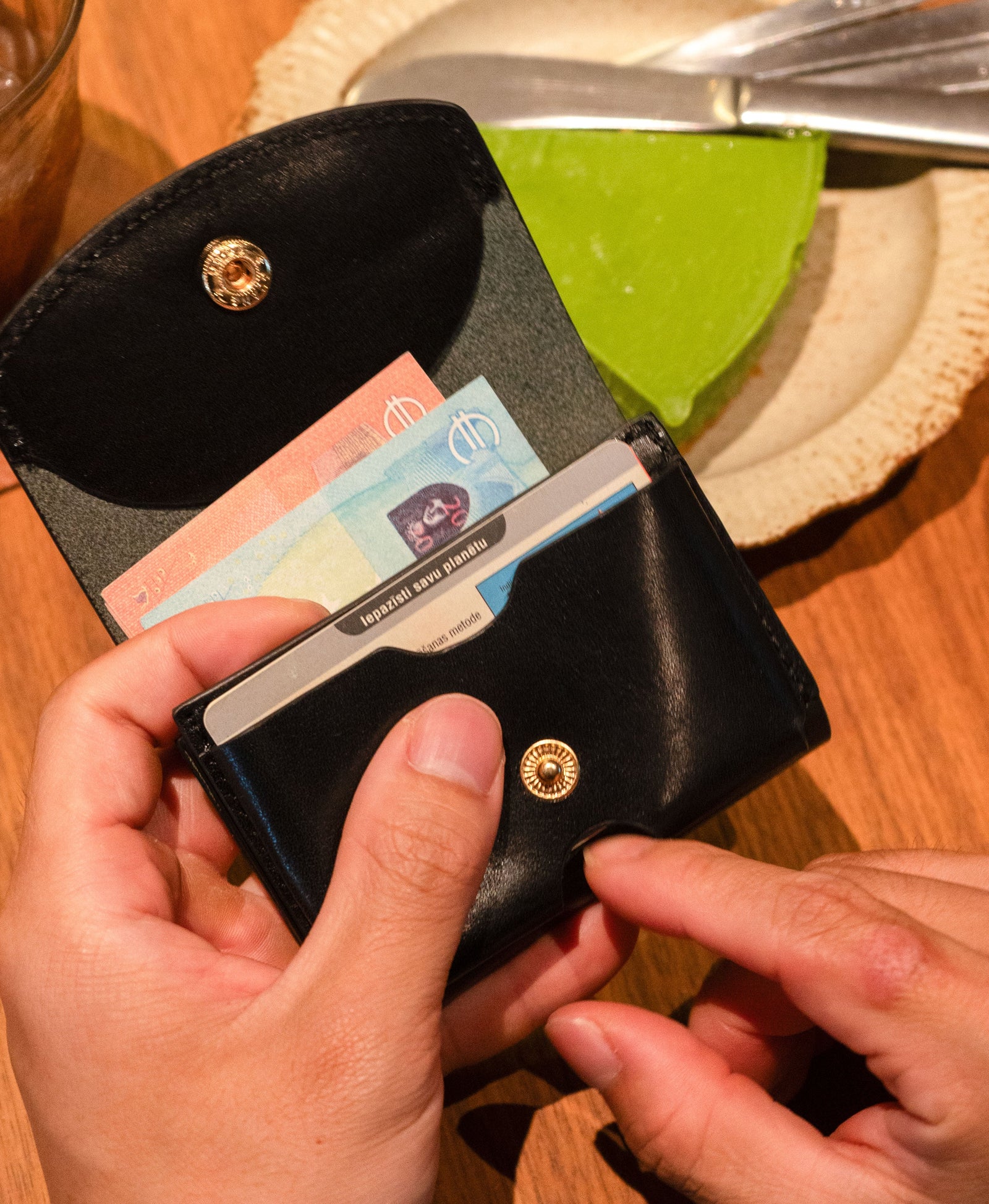 Compact black leather trifold wallet carried by hand