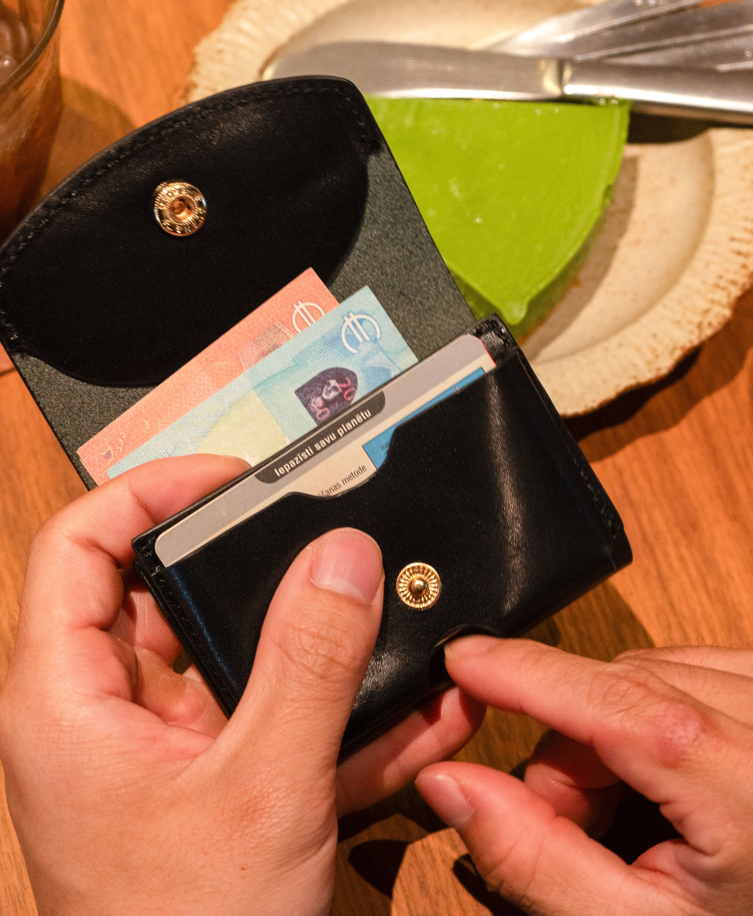 Compact black leather trifold wallet carried by hand