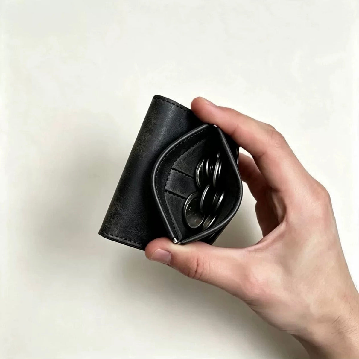 Black trifold wallet held with spring-open coin pocket and coins