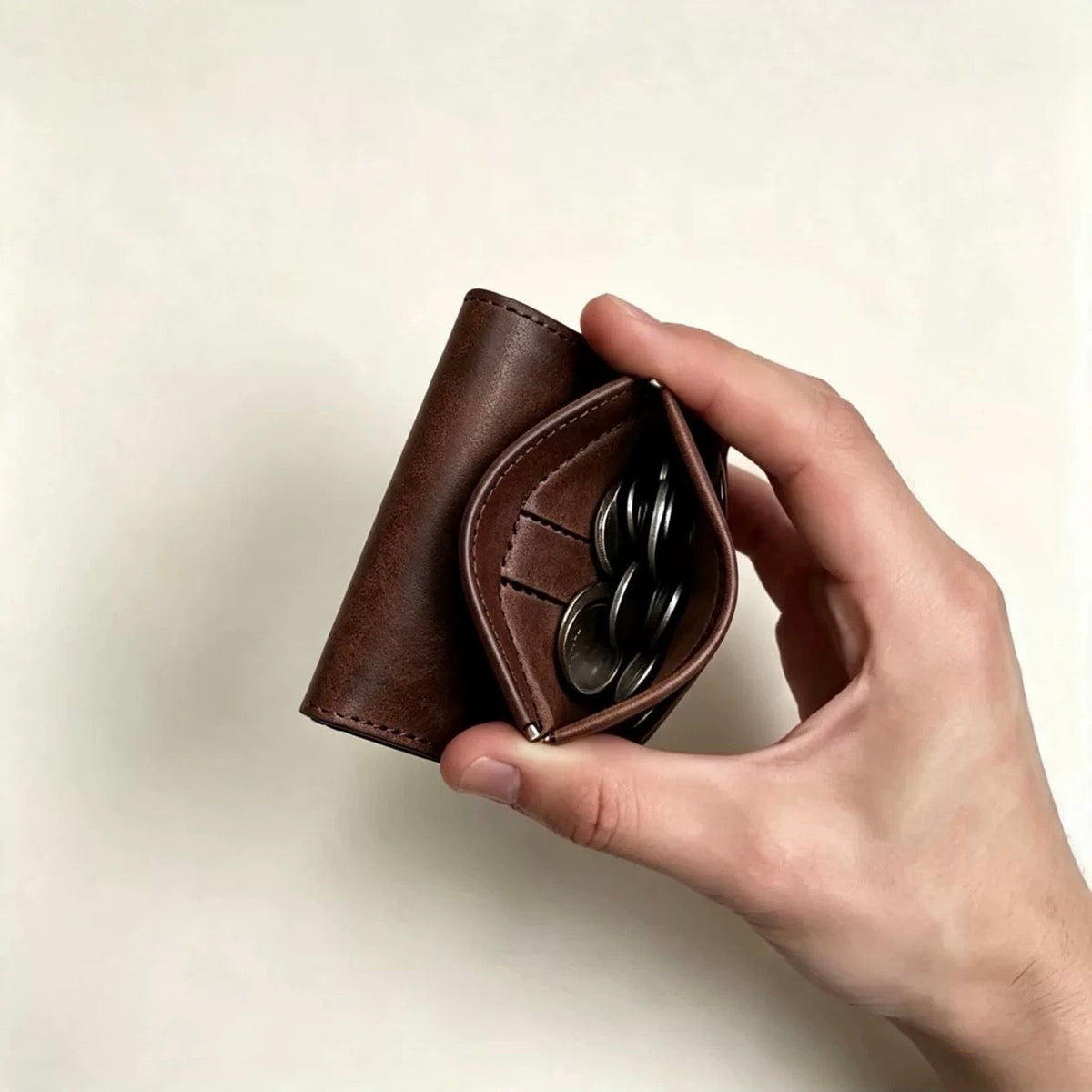 Brown trifold wallet held with spring-open coin pocket and coins
