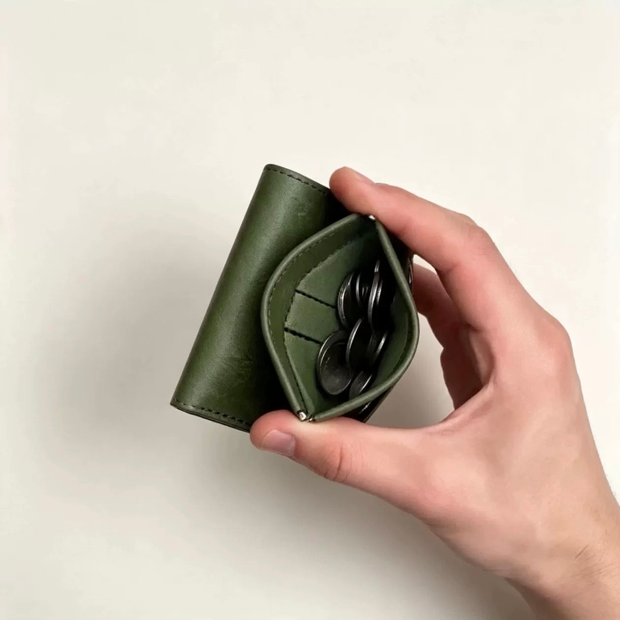Green trifold wallet held with spring-open coin pocket and coins