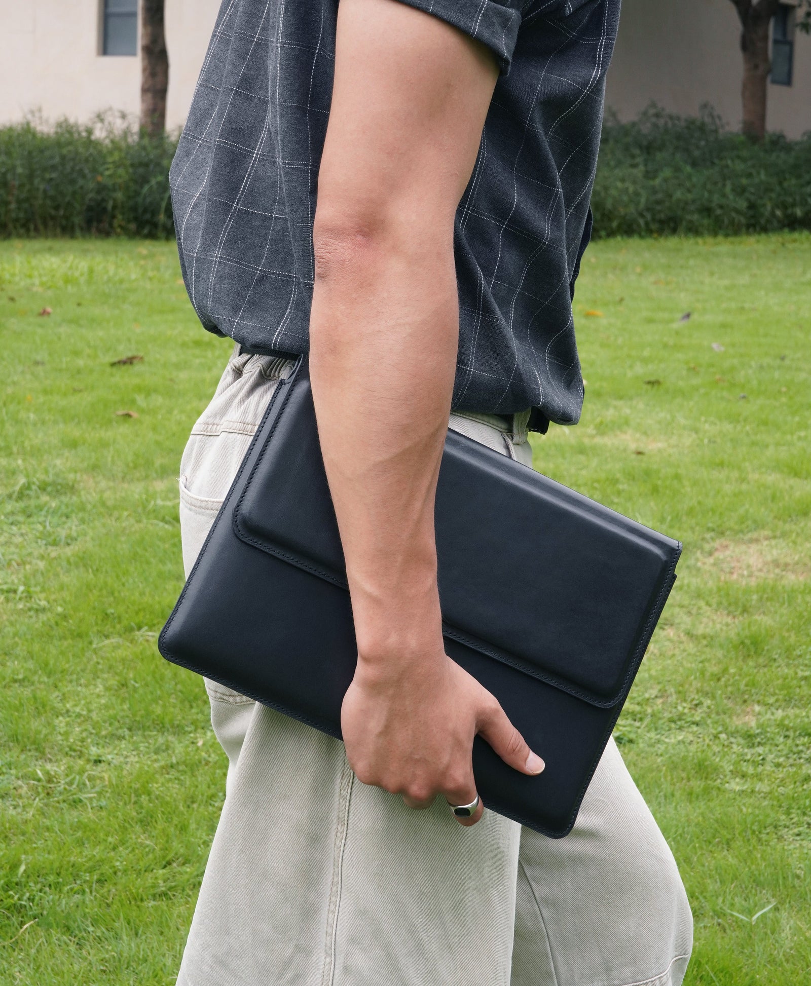 Black full-grain bridle leather laptop sleeve carried by hand outdoors