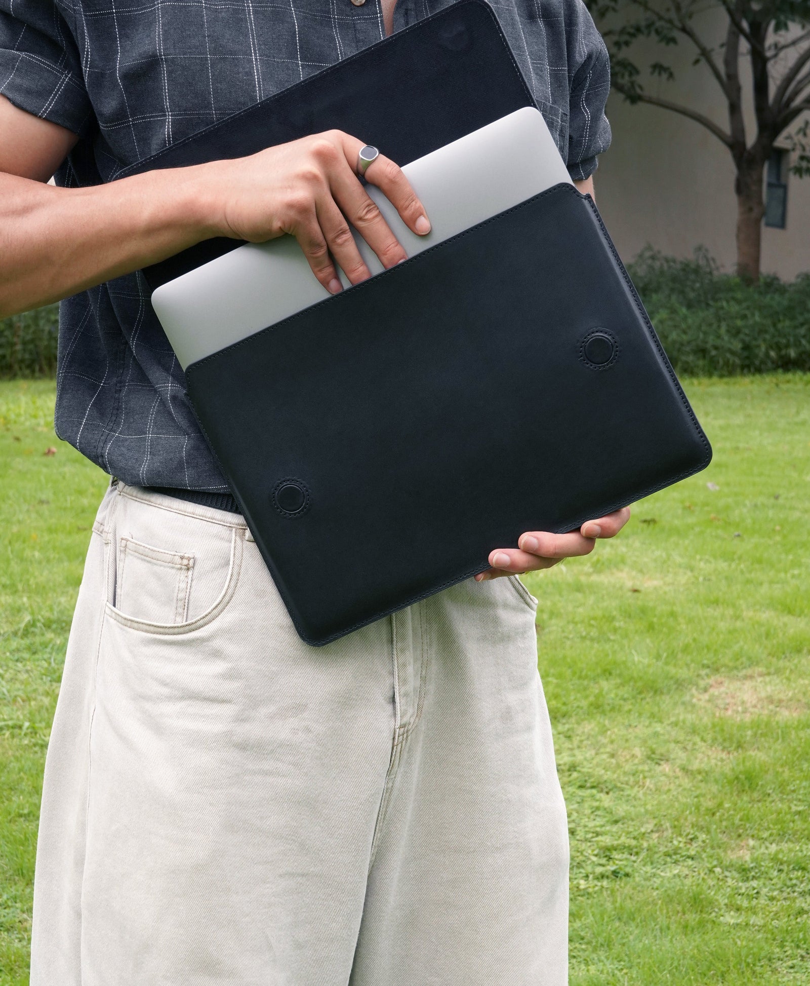 Black full-grain bridle leather laptop sleeve with MacBook being inserted outdoors
