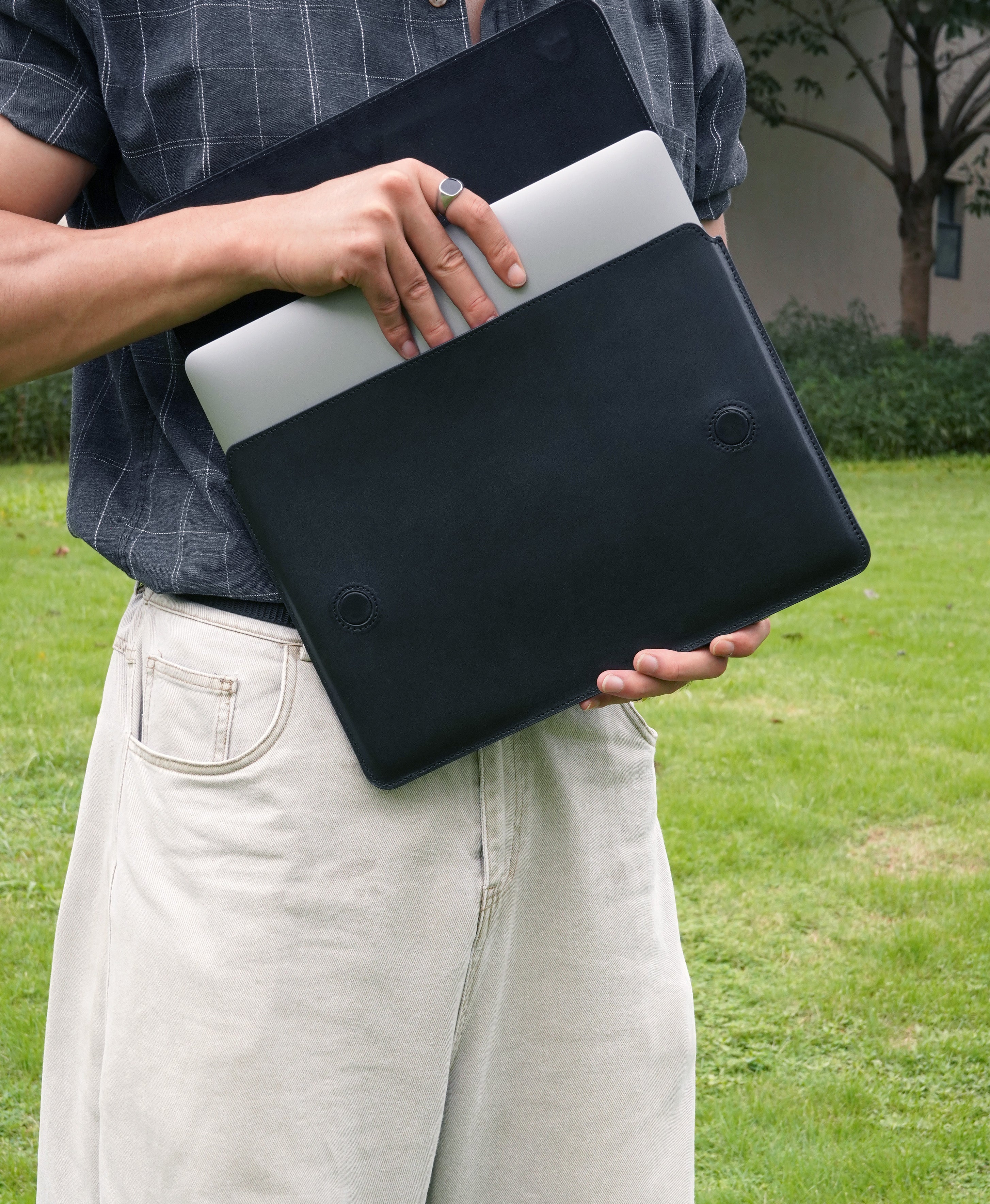 Black full-grain bridle leather laptop sleeve with MacBook being inserted outdoors