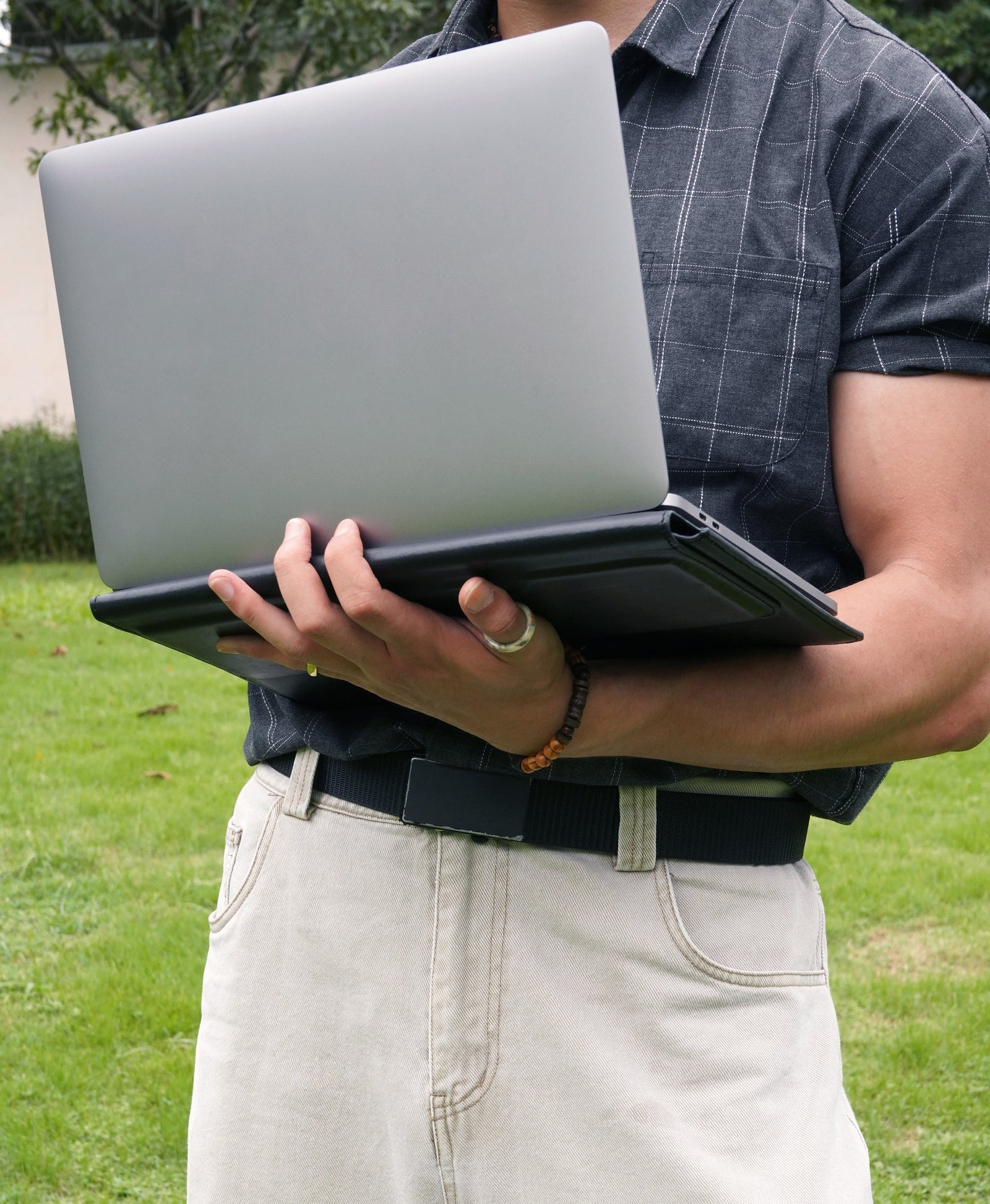Black leather laptop sleeve folded into a stand while holding an open MacBook outdoors
