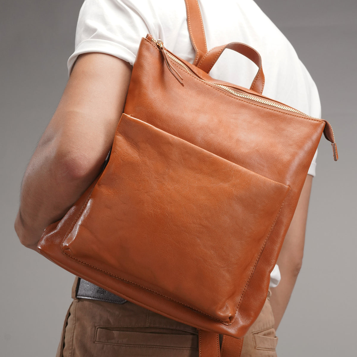 Tan full-grain leather backpack worn on the back at an angle