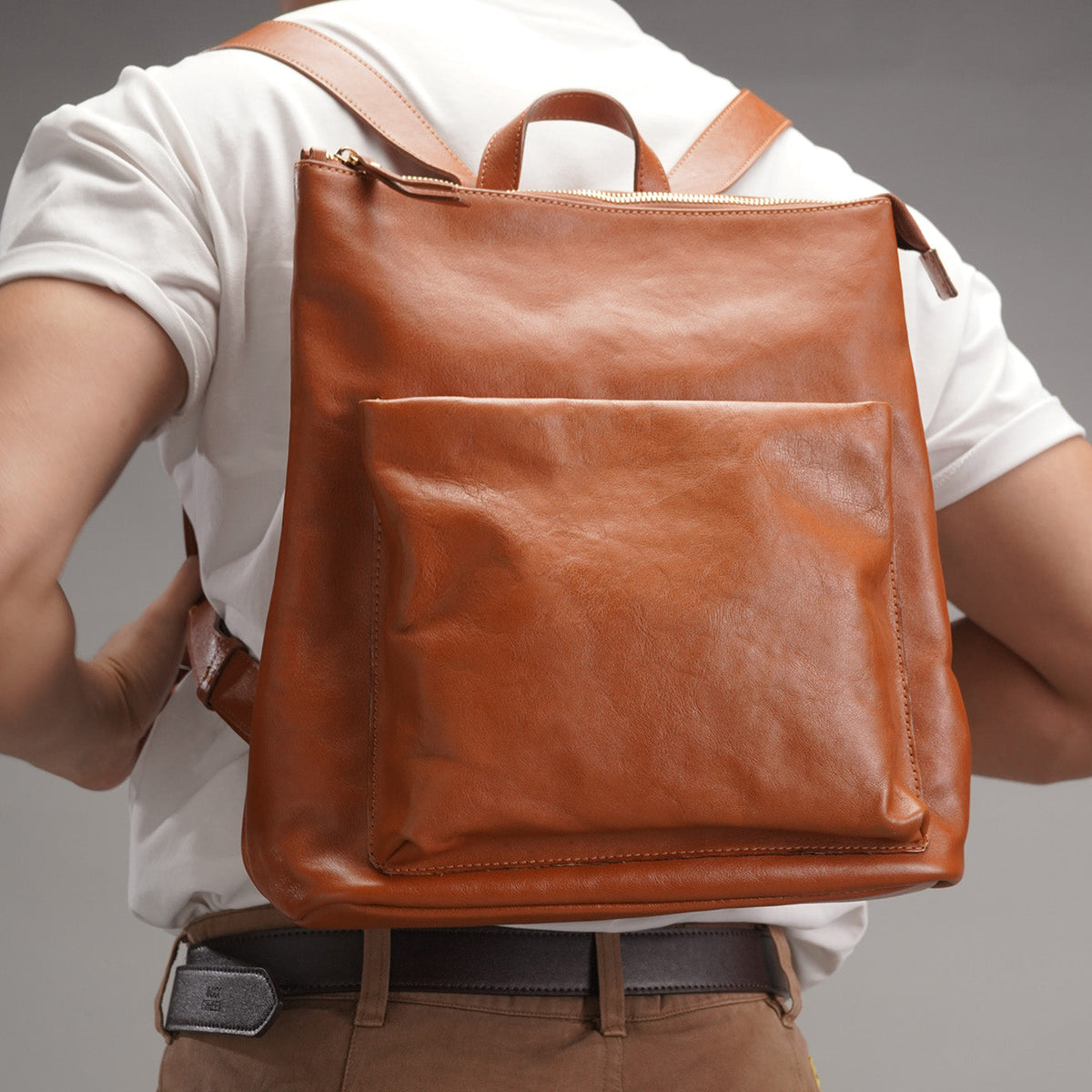 Tan full-grain leather backpack worn on the back, front view