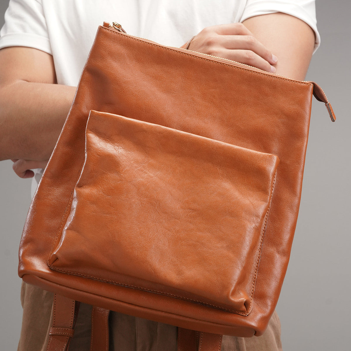 Hand reaching into the main top zip compartment of the leather backpack