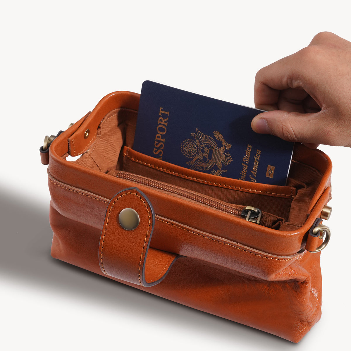 Compact leather crossbody bag shown with a passport for scale
