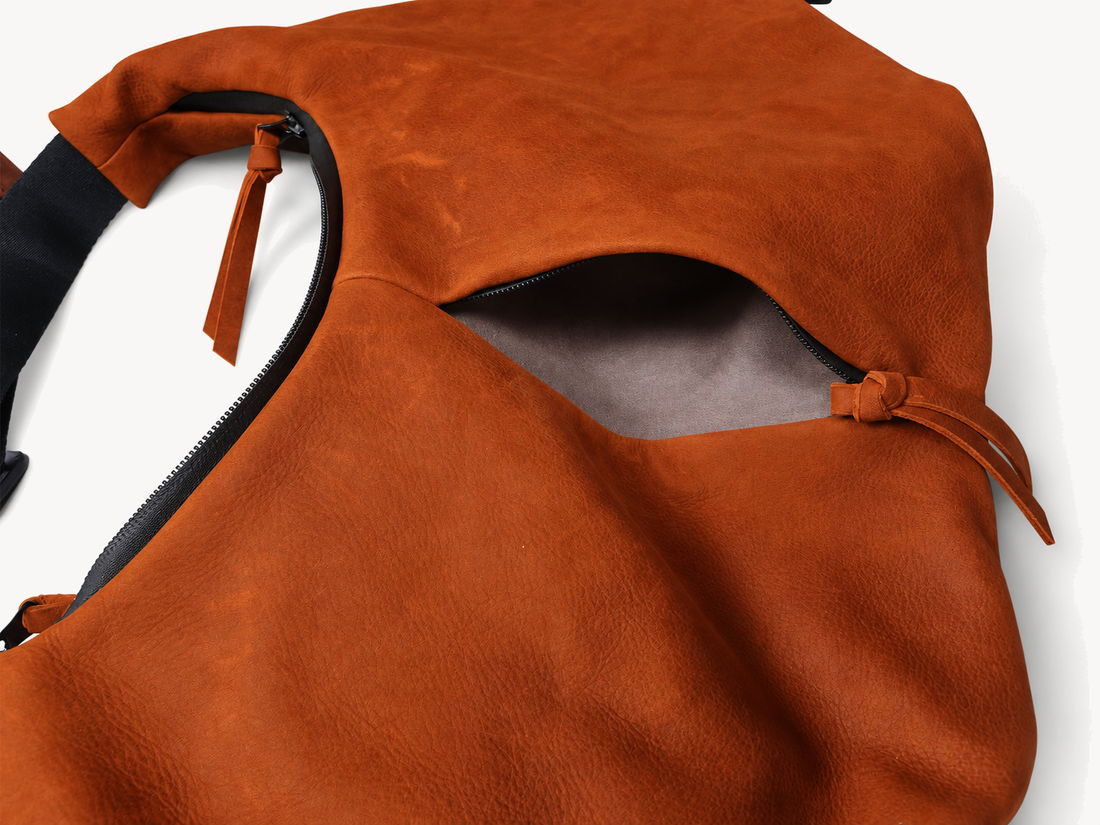 Close view of an exterior zip opening on the orange cowhide crossbody bag