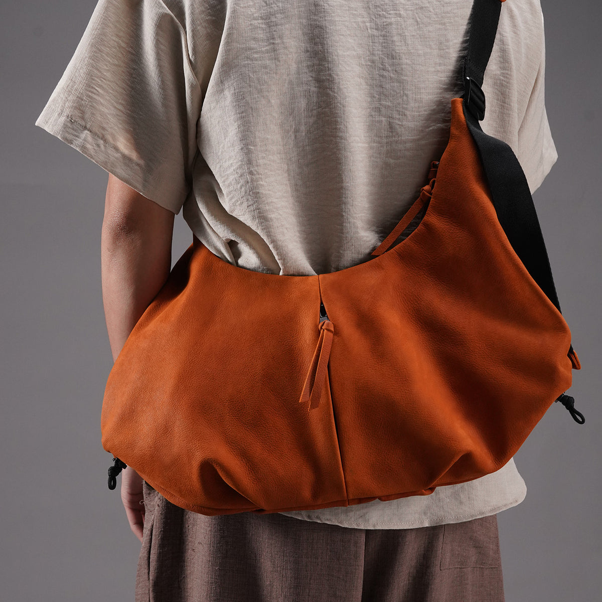 Wide front view of the orange cowhide utility crossbody bag being worn