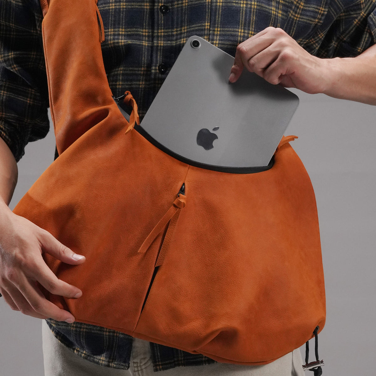 Tablet being placed into the roomy main compartment of the orange cowhide bag