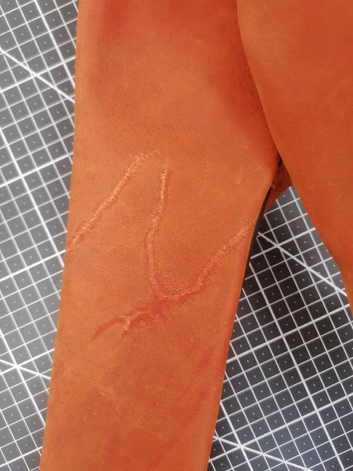 Natural healed marking and grain variation visible on orange cowhide before assembly