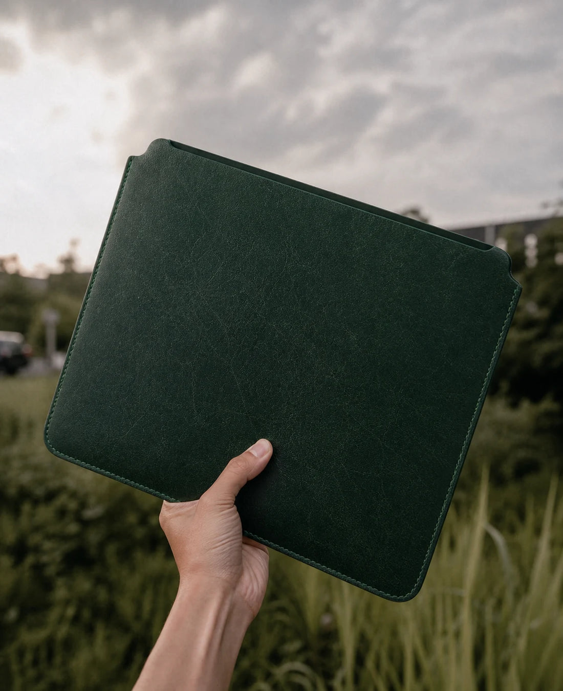 Forest green leather iPad and MacBook sleeve held outdoors with visible open top edge
