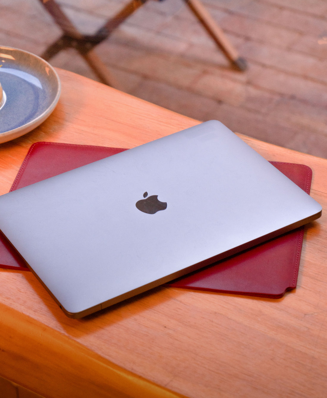 Red full-grain leather MacBook sleeve used beneath a laptop at a cafe table